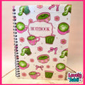 A spiral-bound notebook with a white cover decorated with pink and green illustrations of coffee cups, cupcakes, bows, and flowers, featuring a central label that reads 'NOTEBOOK'.