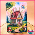 A colorful illustrated tin sign or plaque featuring a whimsical cottage scene with a red roof, green trees, flowers, mushrooms, and a spiral moon, displayed on a wooden surface with a pink border and a 'Lovely Subli' logo in the corner.