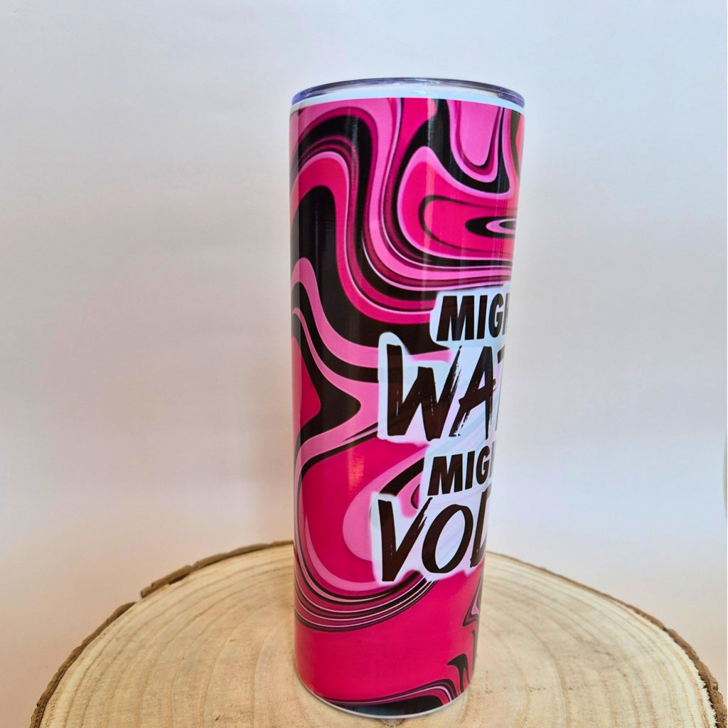 A tall insulated tumbler with a vibrant pink, black, and white marbled swirl pattern and bold text reading 'Mighty Water Volume' in white and black, displayed on a round wooden slice against a plain light background.