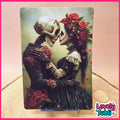 A vertical art print featuring a Day of the Dead style couple with a skeleton and a woman with red roses in a black dress, displayed on a wooden surface with a pink border and a 'Lovely Subli' logo in the corner.