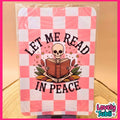 A square printed sign or sticker featuring a pink and white checkered background with an illustration of a skeleton reading a book, surrounded by the words “LET ME READ IN PEACE.” The item is photographed inside a clear plastic sleeve, standing on a small black base against a warm beige background.