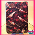 A rectangular art print or card featuring a dark, bloody scene with multiple knives and red splatter, displayed on a small stand against a light wood surface. The print has a white border and a 'Lovely Subli' logo in the bottom right corner.