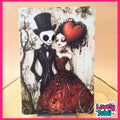 A gothic-style art print featuring a skeleton man in a black top hat and tuxedo next to a woman in a red dress with a large red heart on her head, displayed on a wooden surface with a pink border and 'Lovely Subli' logo.