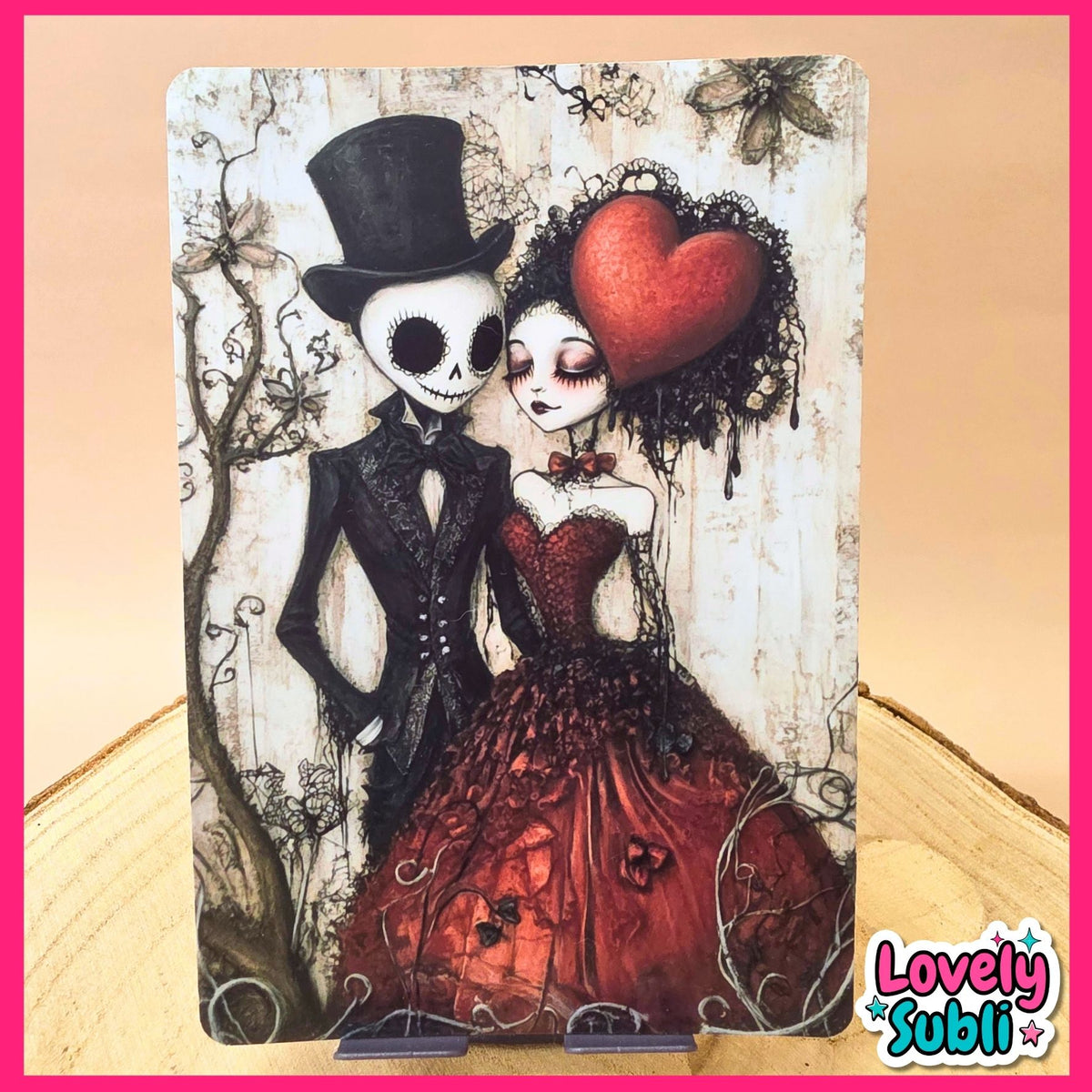 A gothic-style art print featuring a skeleton man in a black top hat and tuxedo next to a woman in a red dress with a large red heart on her head, displayed on a wooden surface with a pink border and 'Lovely Subli' logo.