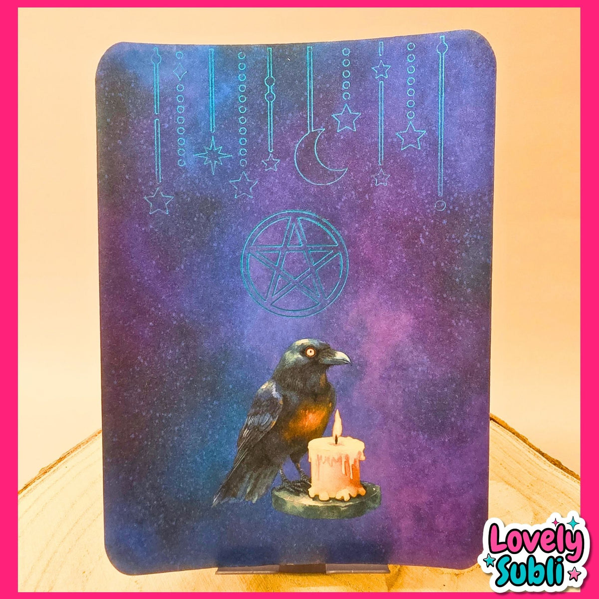 A square art print or card featuring a dark raven perched on a lit candle against a purple and blue starry sky with a crescent moon and pentagram, displayed on a stand with a pink border around the image.