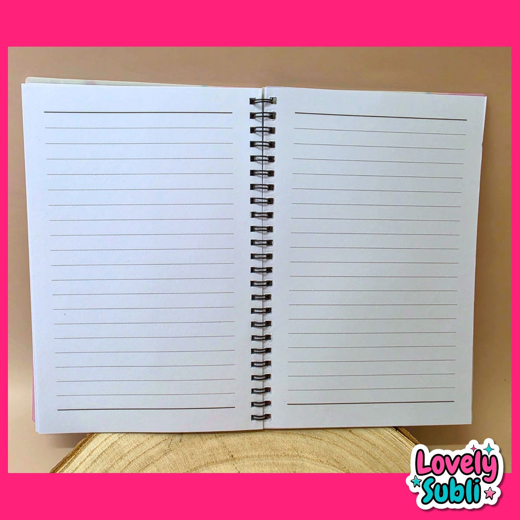 An open spiral-bound lined notebook or planner pad displayed upright on a wooden surface against a tan background, with a bright pink border and a 'Lovely Subli' logo in the bottom right corner.