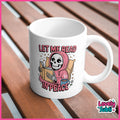 A white ceramic mug with a cartoon grim reaper reading in a pink hoodie and the text 'LET ME READ IN PEACE' on the side, placed on a brown wooden slatted surface.