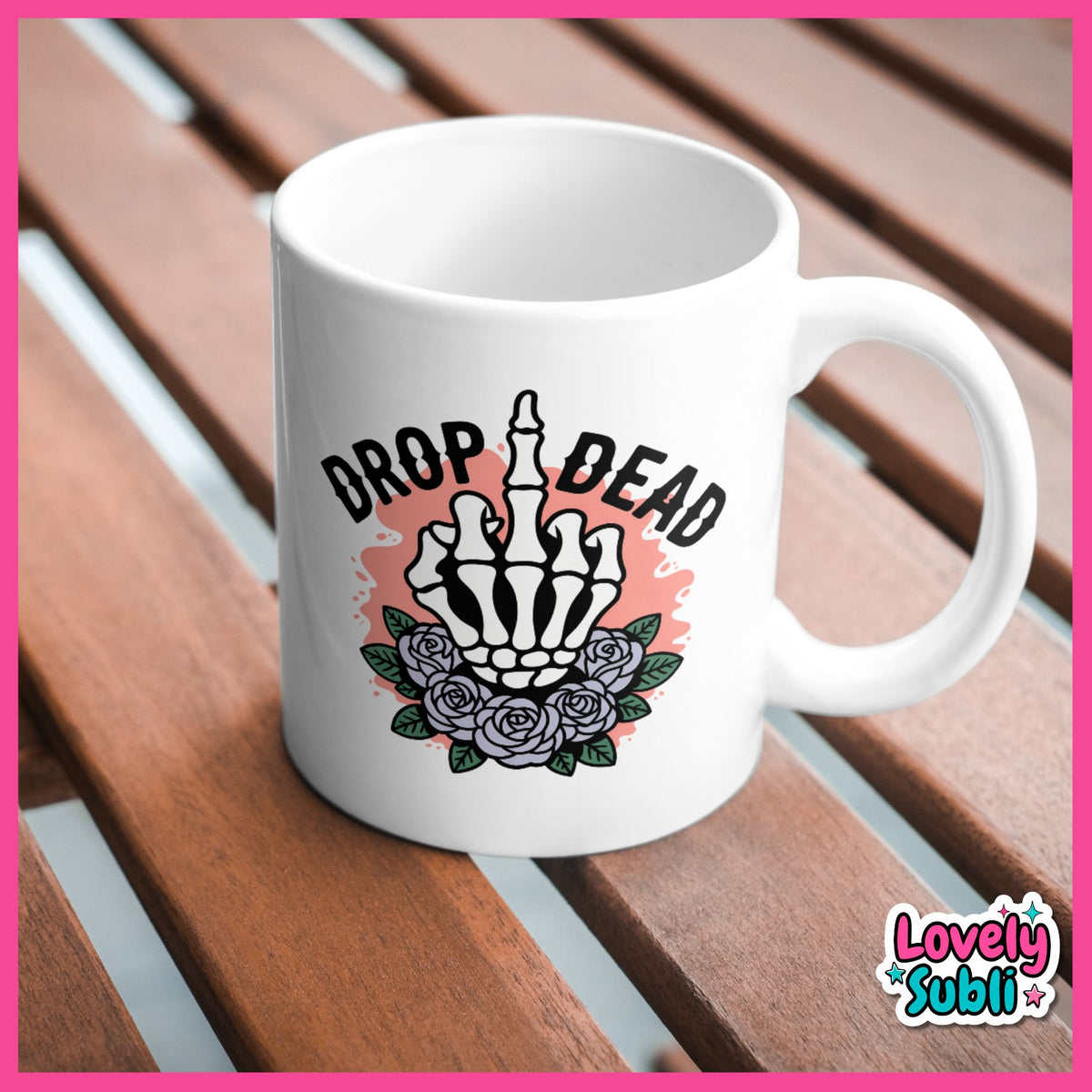 A white ceramic mug with a 'Drop Dead' skeleton hand and roses graphic, resting on a brown wooden slatted surface.