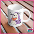 A white ceramic mug with a cute cartoon ghost illustration reading an orange book under a purple blanket with black stars, placed on a brown wooden slatted surface. The mug has a 'Lovely Subli' brand watermark in the bottom right corner.