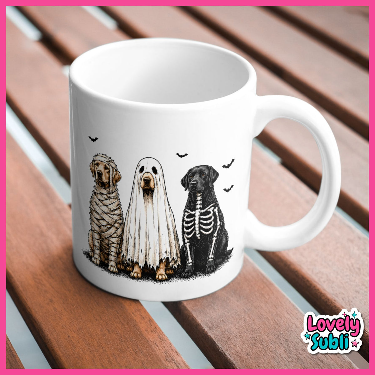 A white ceramic mug featuring a Halloween-themed illustration of three dogs dressed as a mummy, a ghost, and a skeleton, sitting on a brown wooden slatted surface. The mug is framed by a pink border, with a 'Lovely Subli' brand logo in the bottom right corner.