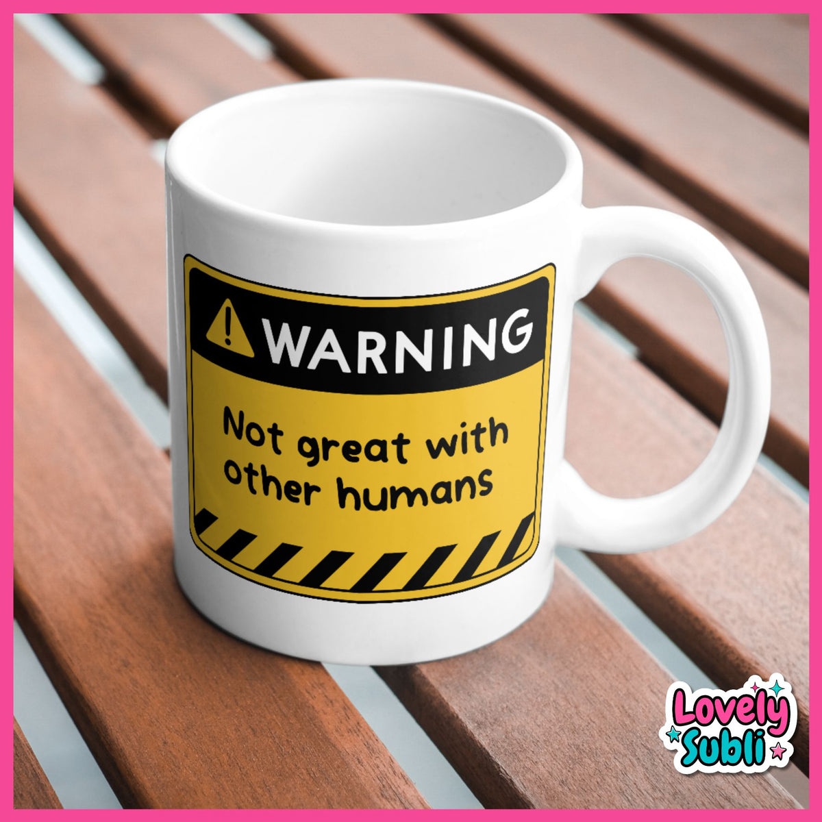 A white ceramic mug with a humorous warning label graphic that reads 'WARNING Not great with other humans' in black and yellow, placed on a brown wooden slatted surface.