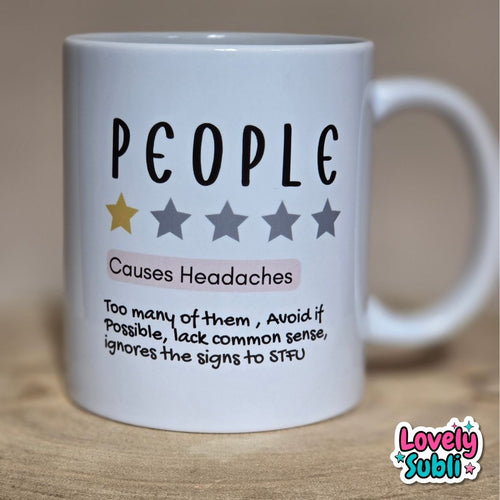 A white ceramic mug printed with the word 'PEOPLE' in black, five stars (one gold, four gray), the phrase 'Causes Headaches' in black and pink, and a humorous definition below. The mug is photographed on a wooden surface with a warm beige background.