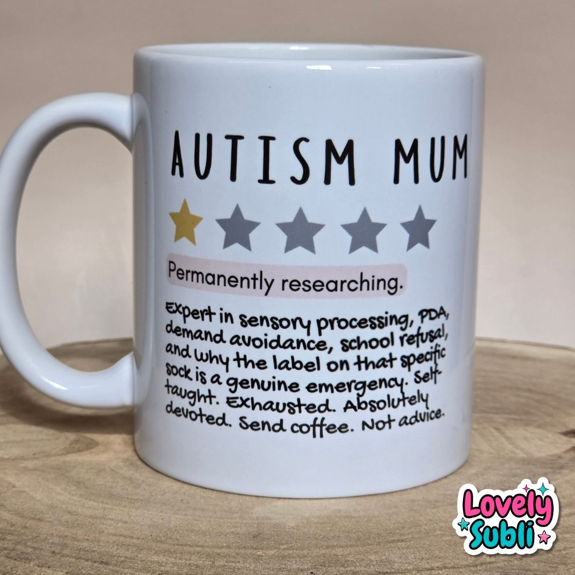 A white ceramic mug printed with the words 'AUTISM MUM' and a humorous list of traits, placed on a wooden surface against a beige background.