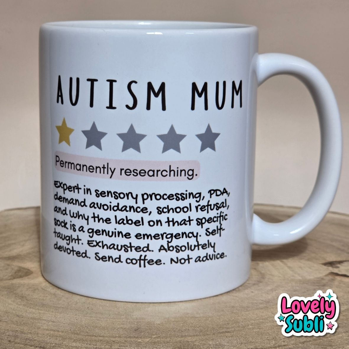 A white ceramic mug printed with the words 'AUTISM MUM' and a humorous definition-style text block, shown on a wooden surface with a neutral background. A 'Lovely Subli' watermark appears in the bottom right corner.