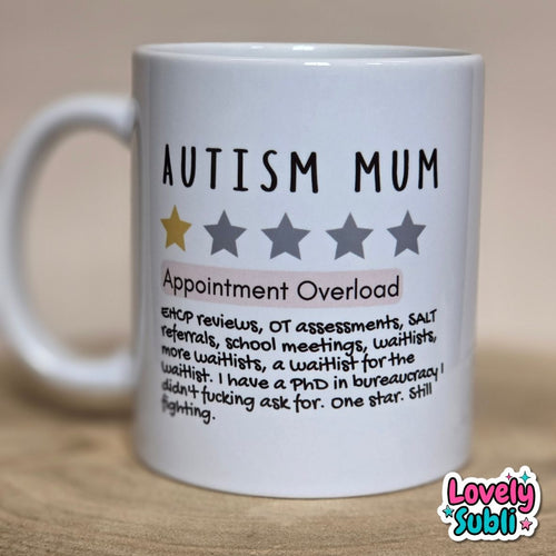 A white ceramic mug printed with the words 'AUTISM MUM' and a humorous definition of 'Appointment Overload' under a pink highlight bar. The mug is photographed on a wooden surface against a neutral beige background.
