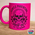 A bright hot pink ceramic mug with a black graphic of a skull, flowers, and the text 'GENTLE PARENTING DROP OUT EST: THIS MORNING' on a wooden surface.