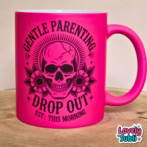 A bright hot pink ceramic mug with a black graphic of a skull wearing ear cuffs, surrounded by flowers and the text 'GENTLE PARENTING DROP OUT EST. THIS MORNING'.