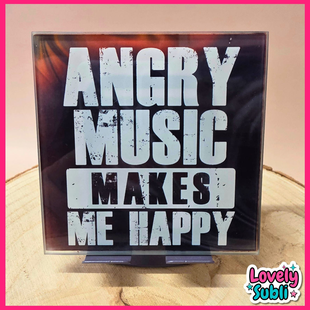 A square acrylic sign with the text 'ANGRY MUSIC MAKES ME HAPPY' in distressed white lettering on a black background, displayed on a small stand on a wooden surface.