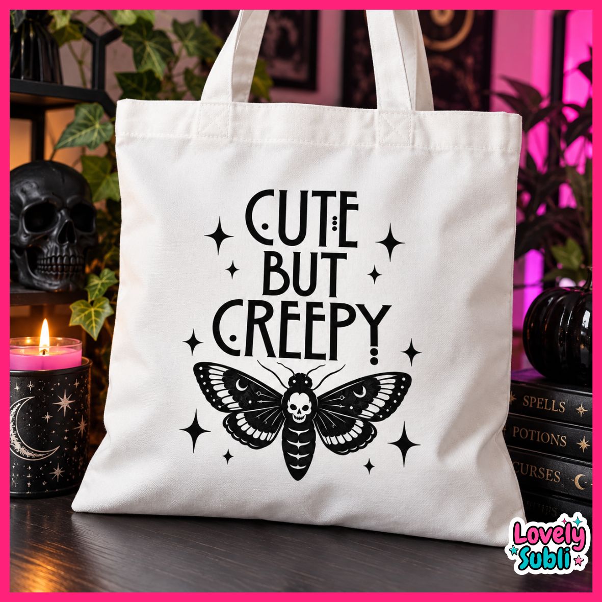 A white canvas tote bag with black printed text reading 'CUTE BUT CREEPY' above a black moth with a skull in the center, displayed on a dark table with gothic-themed props including a skull, candle, and books.