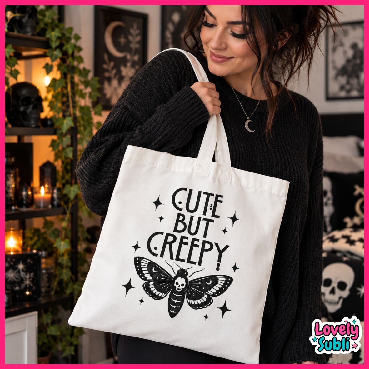 A woman wearing a black knit sweater carries a white canvas tote bag with a black graphic print that reads 'CUTE BUT CREEPY' above a moth illustration. The photo is taken in a dimly lit, gothic-themed room with candles, shelves, and skull decor, framed by a bright pink border.