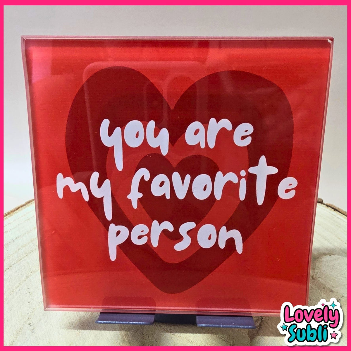 A square acrylic sign with a red background featuring three overlapping heart shapes and the phrase 'you are my favorite person' in white script. The sign is displayed on a small stand on a light surface, with a 'Lovely Subli' watermark in the bottom right corner.