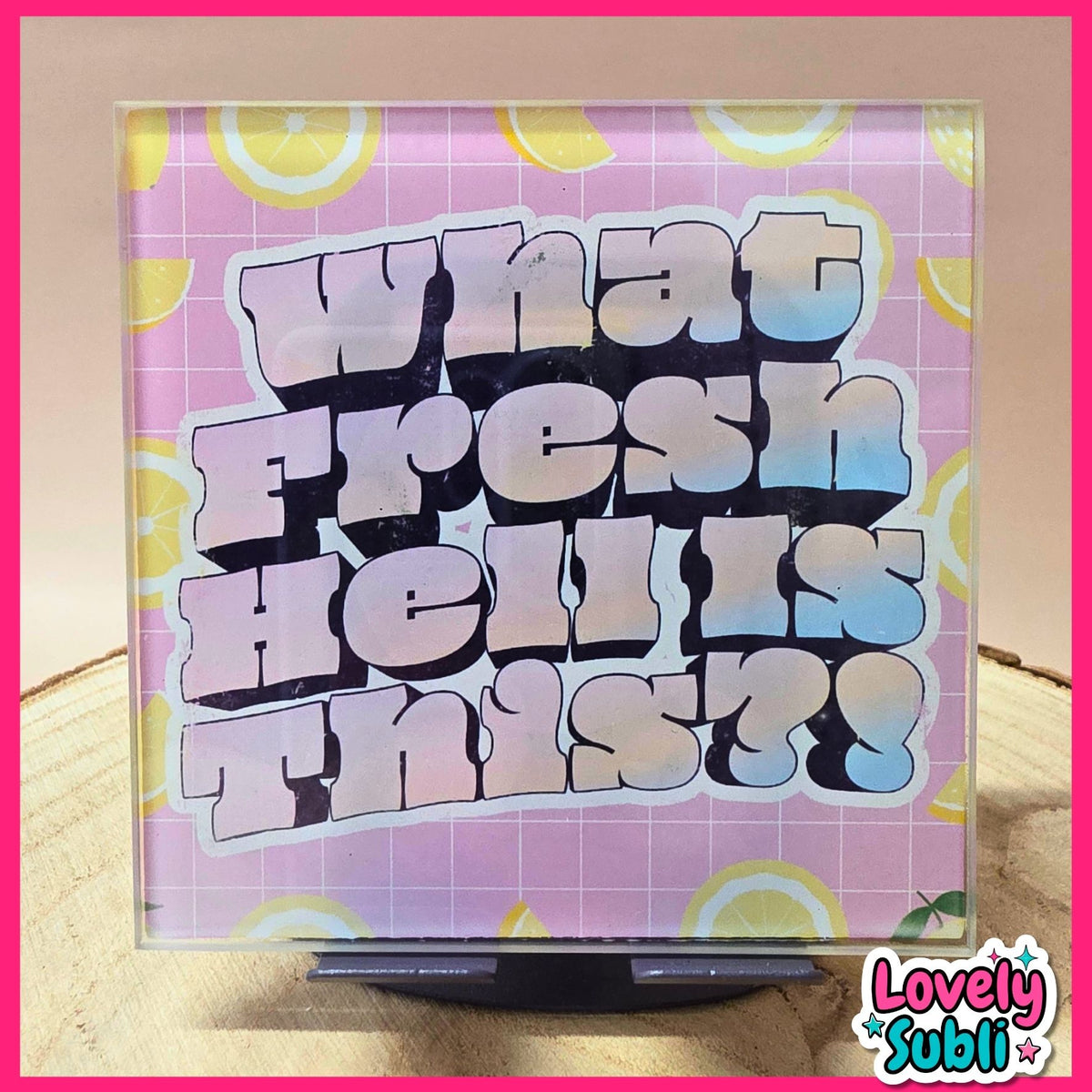 A square acrylic art print featuring the text 'what fresh hell is this?' in a bold, 3D bubble font with a pink-to-blue gradient. The background of the print has a pink grid pattern with yellow lemon slice motifs.
