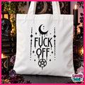 A white canvas tote bag with a black gothic-style graphic reading 'FUCK OFF' with a crescent moon, stars, and pentagram. The bag is displayed in a styled witch-themed setting with candles, a skull, and occult books.