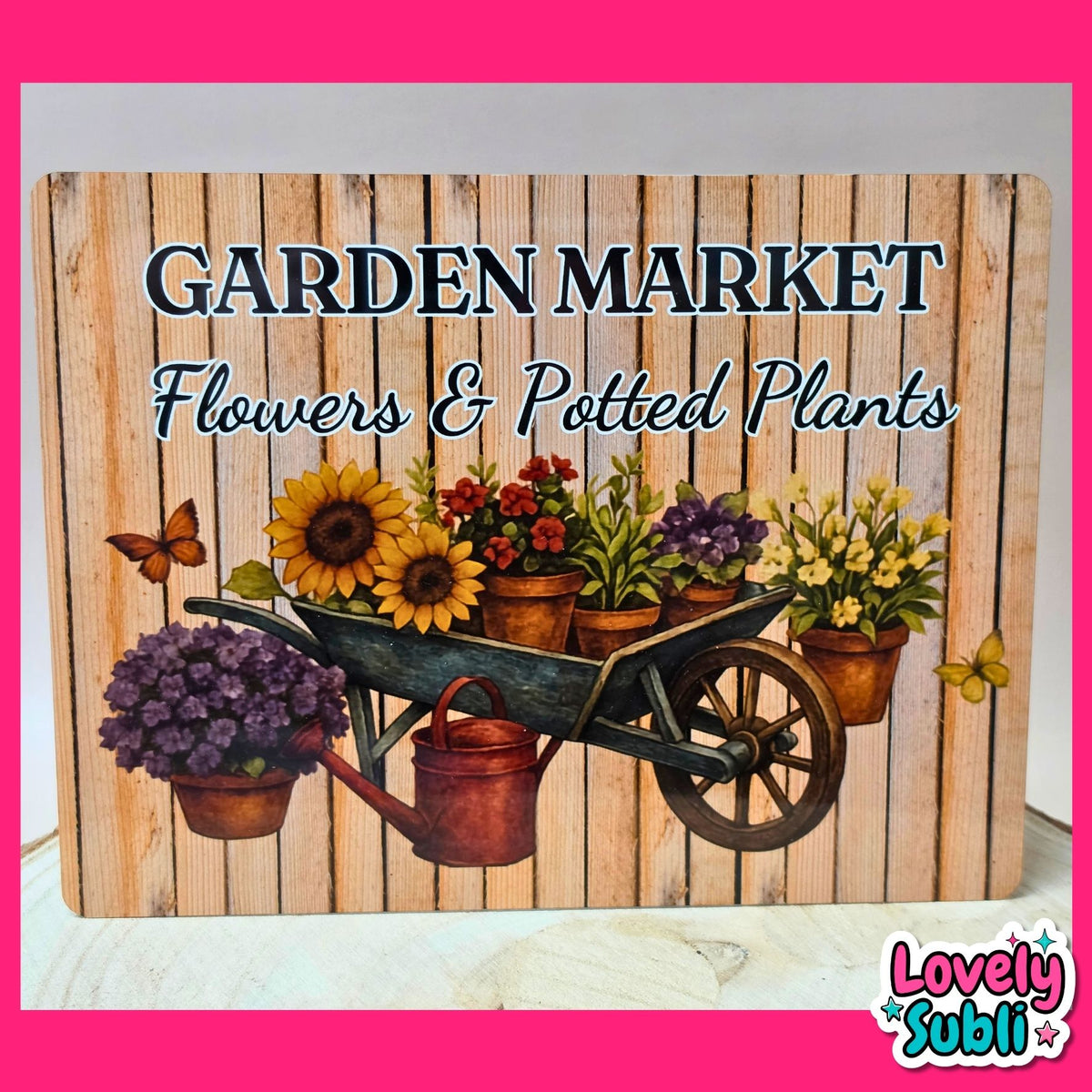 A rectangular decorative sign with a rustic wood-plank background and the text 'GARDEN MARKET Flowers & Potted Plants.' The sign features an illustrated wheelbarrow filled with sunflowers, red flowers, green plants, purple flowers, yellow flowers, a copper watering can, butterflies, and potted plants.