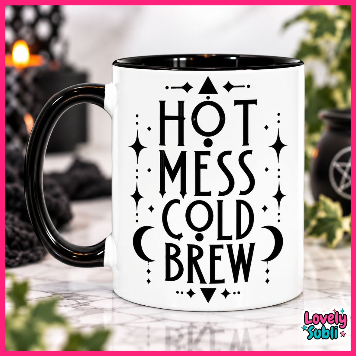 A white ceramic mug with a black handle and black interior, featuring the text 'HOT MESS COLD BREW' in black lettering with decorative symbols. The mug is set against a softly blurred background with a pink border.
