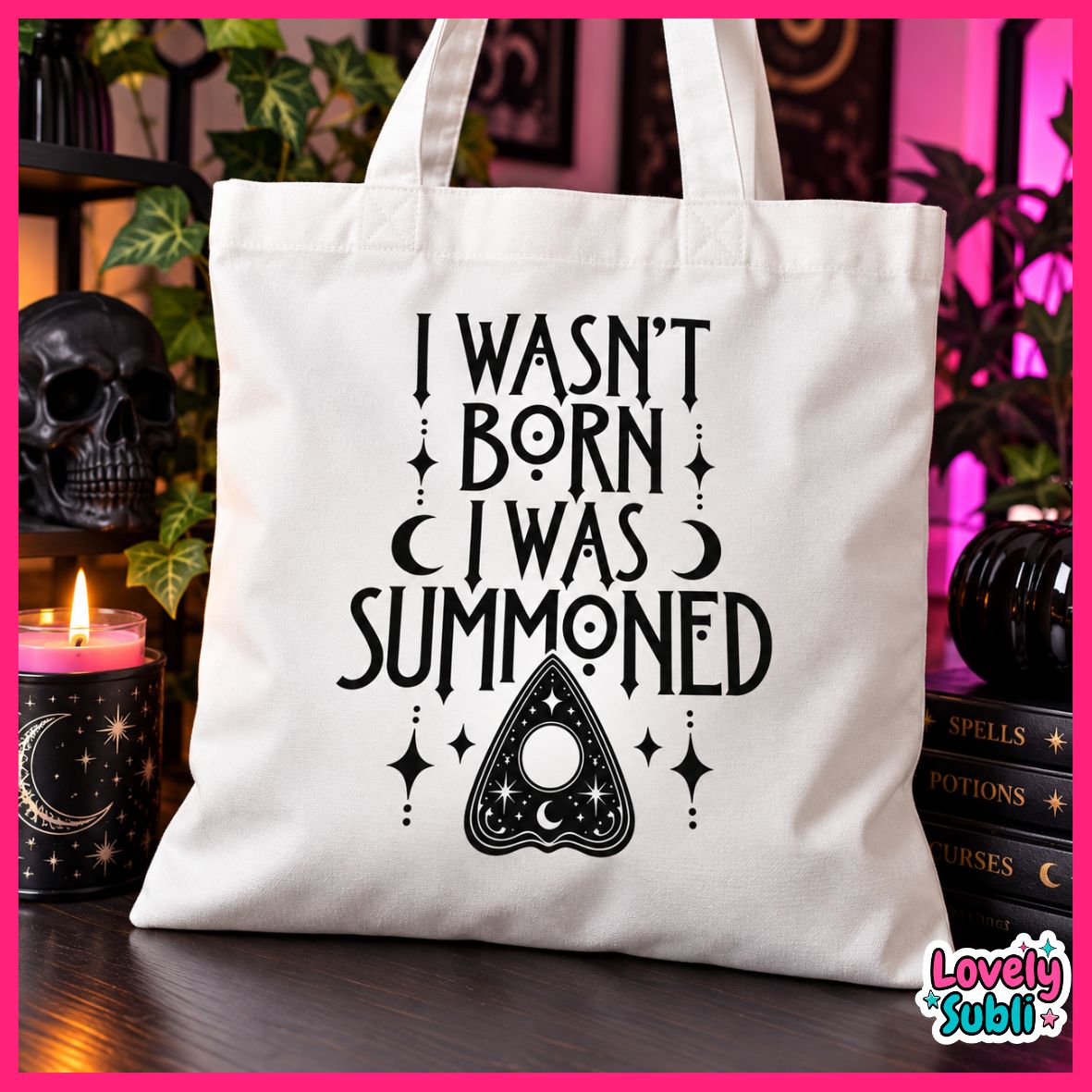 A white canvas tote bag with black gothic-style text reading 'I WASN'T BORN I WAS SUMMONED' and an amulet illustration, displayed on a dark table with candles, books, and plants in a styled setting. A 'Lovely Subli' logo is visible in the bottom right corner.