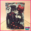 A vertical art print featuring a gothic Victorian-style couple kissing, with red hearts, roses, and a bat against a pale background, displayed on a wooden surface with a pink border and a 'Lovely Subl' logo in the corner.