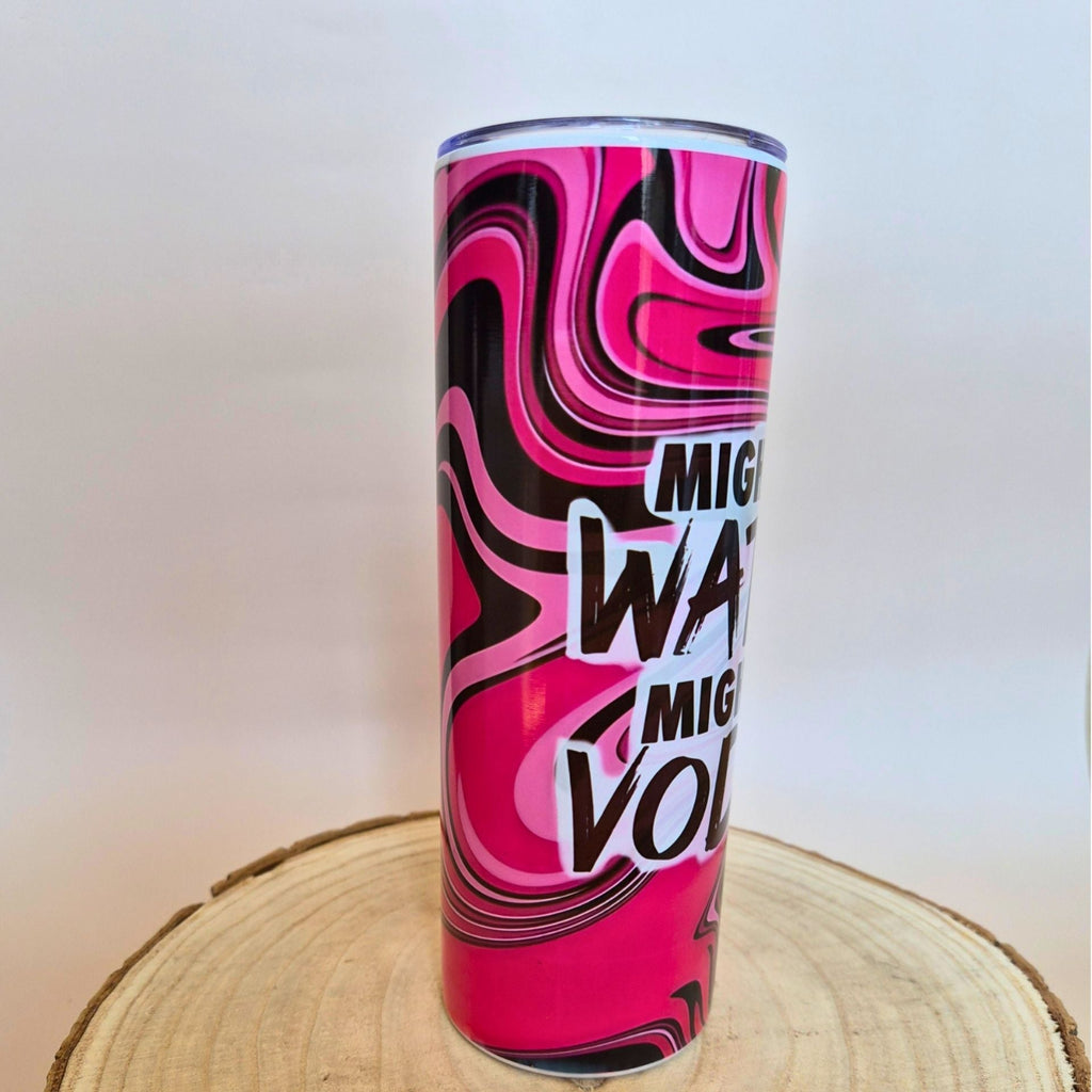 A tall insulated tumbler with a vibrant pink, black, and white marbled swirl pattern and bold text reading 'Mighty Water Volume' in white and black, displayed on a round wooden slice against a plain light background.