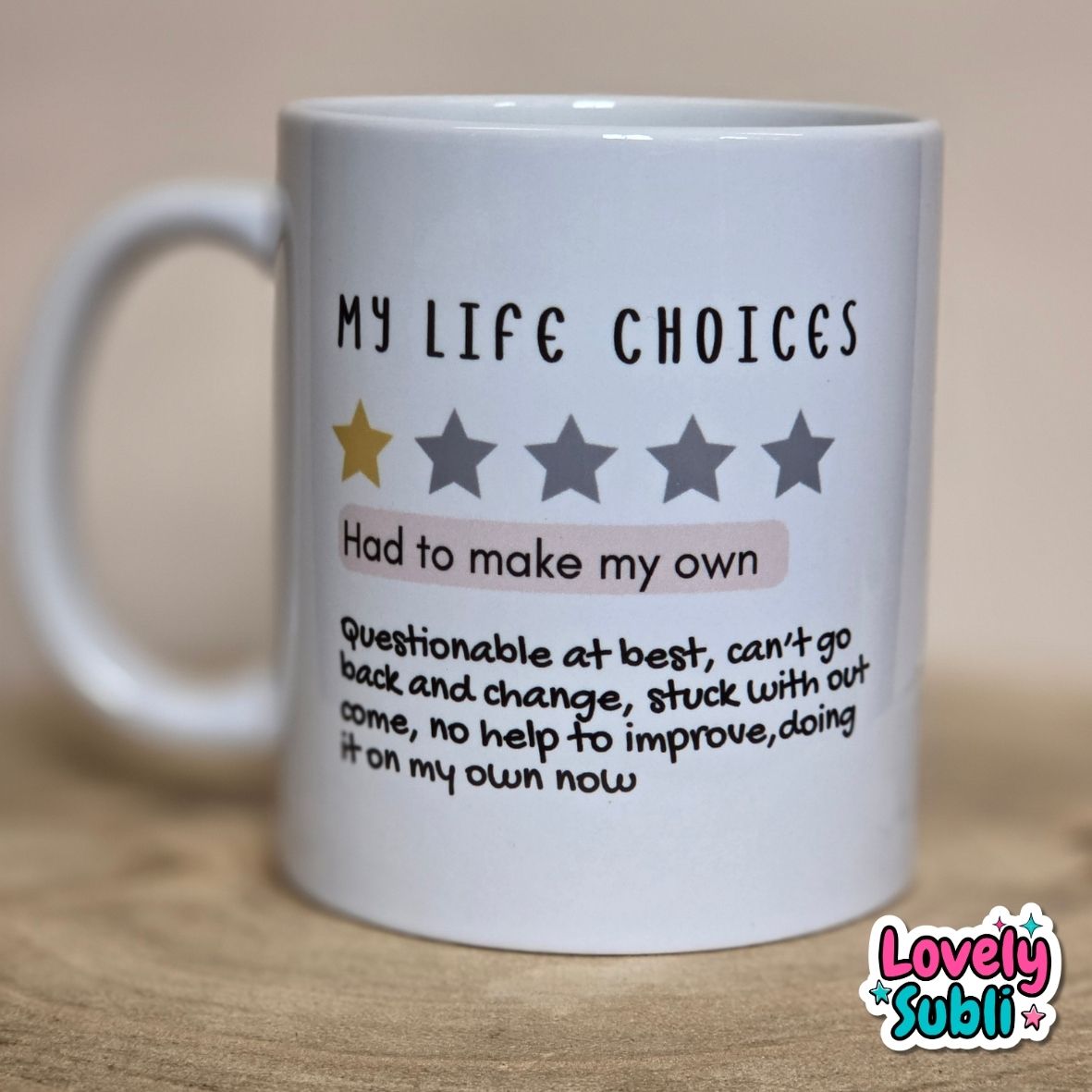 A white ceramic mug with humorous text reading 'MY LIFE CHOICES' and a one-star review graphic, placed on a wooden surface against a neutral beige background.