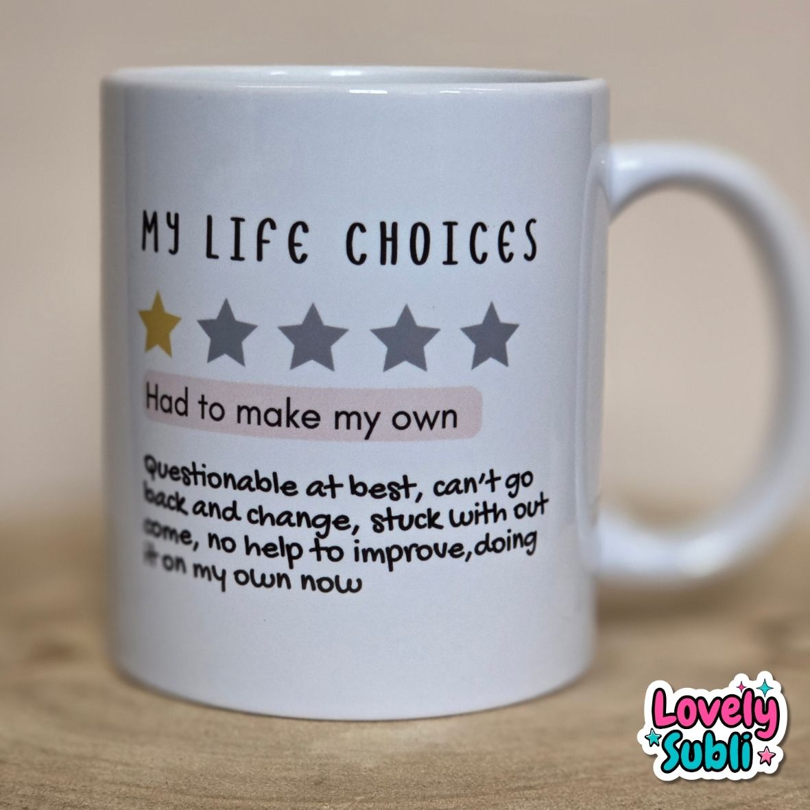 A white ceramic mug with humorous text that reads 'MY LIFE CHOICES' above a one-star rating graphic and a quote starting with 'Had to make my own'. The mug is photographed on a wooden surface against a neutral beige background.