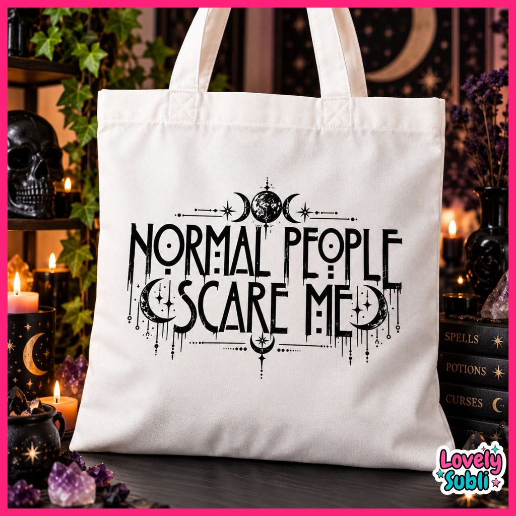 A white canvas tote bag with black gothic-style text reading 'NORMAL PEOPLE SCARE ME' and moon/sun symbols, photographed in a dark, mystical room with candles, crystals, and books.