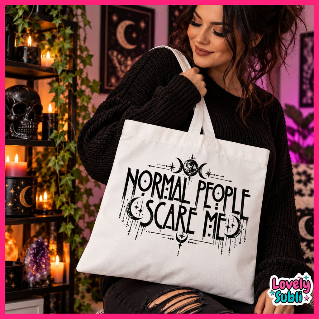 A woman in a black sweater holds a white canvas tote bag with black gothic text reading 'NORMAL PEOPLE SCARE ME' and moon-phase graphics. The setting is a dimly lit, mystical room with candles, a skull, and hanging moon decorations.