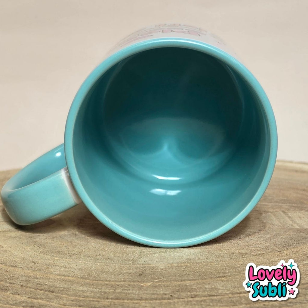 A turquoise ceramic mug shown from a top-down angle, resting on a wooden surface against a neutral beige background. A 'Lovely Subli' brand logo is visible in the bottom right corner.