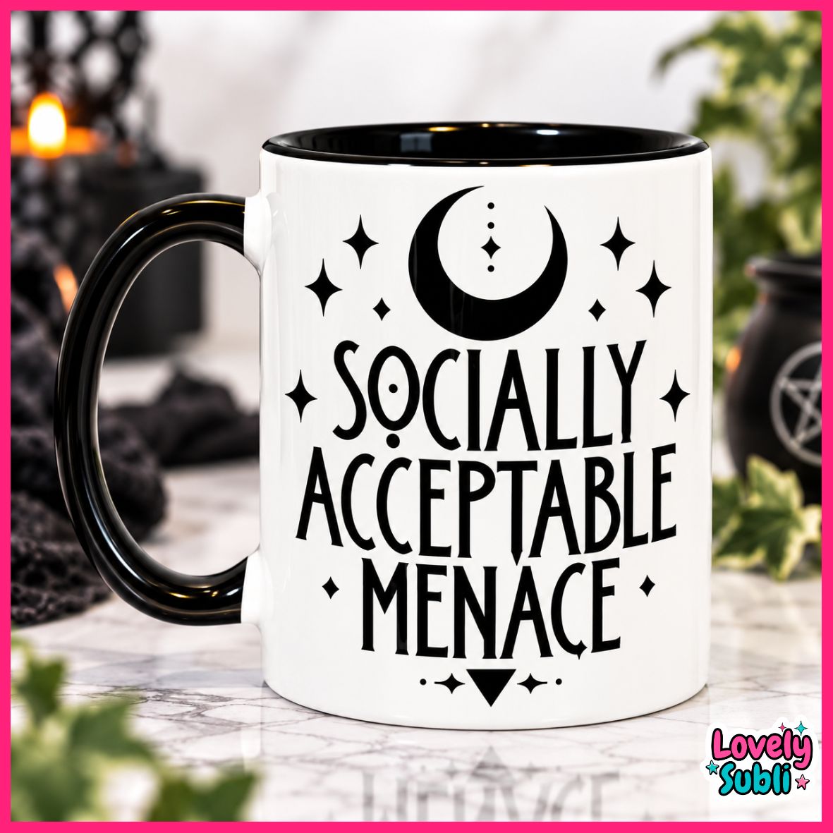 A white ceramic mug with a black handle and black interior, featuring the text 'SOCIALLY ACCEPTABLE MENACE' in black lettering with a crescent moon and stars above. The mug is set on a marble surface with a blurred background containing candles and greenery.