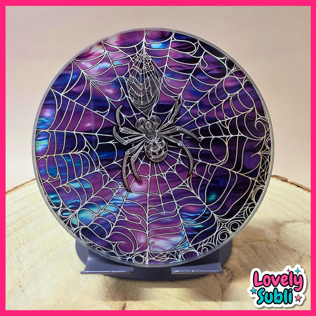 A round decorative plaque or clock face featuring a spiderweb design over a purple and blue iridescent shell-like background, with a metallic spider in the center, displayed on a stand.