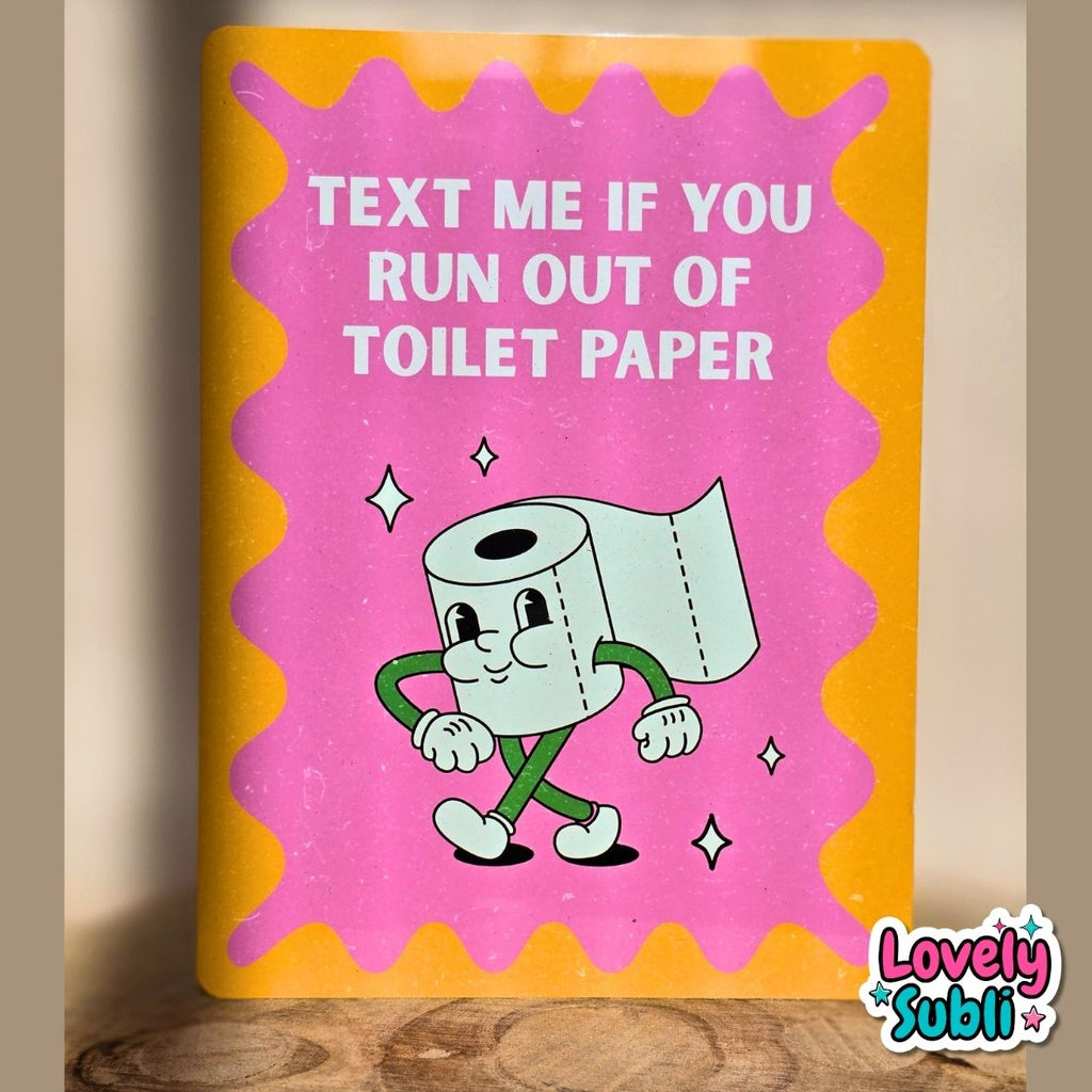 A rectangular novelty sign with a bright yellow border and a pink center, featuring a cartoon toilet paper roll and the text 'TEXT ME IF YOU RUN OUT OF TOILET PAPER.' The sign is photographed leaning against a beige wall on a wooden surface, with a 'Lovely Subli' watermark in the bottom right corner.