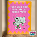 A rectangular novelty sign with a bright yellow border and a pink center, featuring a cartoon toilet paper roll and the text 'TEXT ME IF YOU RUN OUT OF TOILET PAPER.' The sign is photographed leaning against a beige wall on a wooden surface, with a 'Lovely Subli' watermark in the bottom right corner.