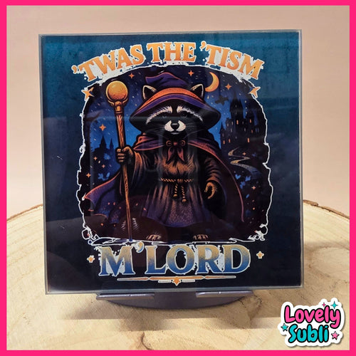 A square printed sign or album-cover-style artwork on a small stand, featuring a raccoon dressed as a wizard holding a staff against a dark blue night scene. The text reads "'Twas the 'Tism" at the top and "M'Lord" at the bottom.