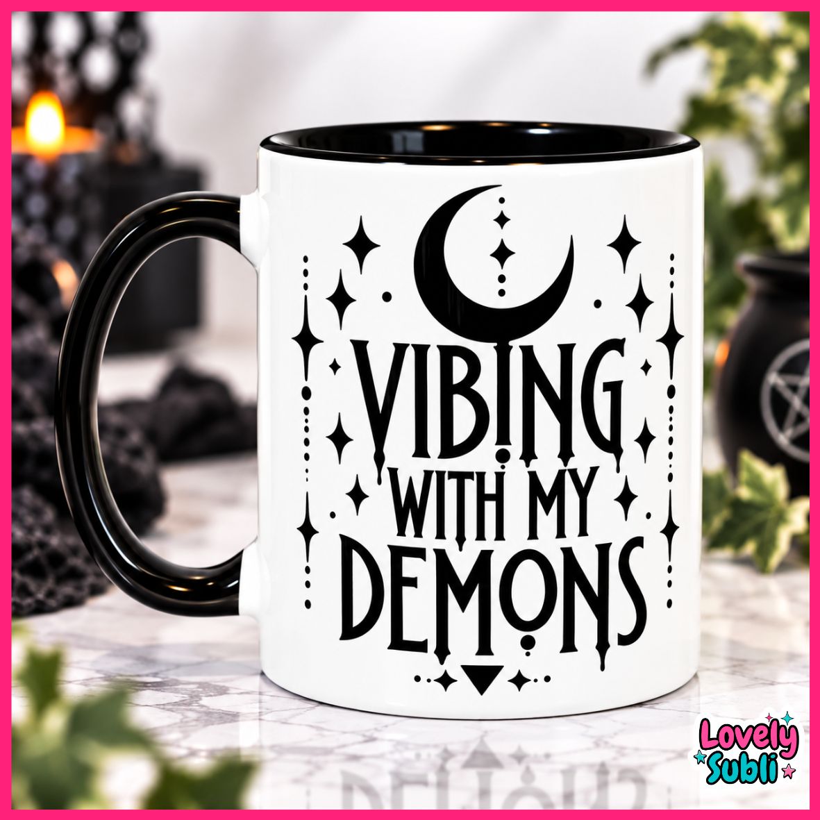 A white ceramic mug with a black handle and black interior, printed with the phrase 'VIBING WITH MY DEMONS' in black lettering alongside a crescent moon and star motifs. The mug is shown on a marble-like surface with a blurred gothic-themed background.